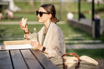 Wall Mural - Young woman having a snack with pizza sitting outdoors at the modern public park