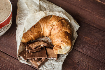 Cup of coffee with fresh croissant and chocolate bars for breakfast