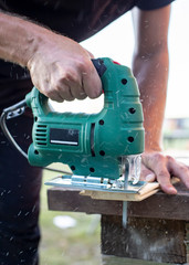 Man cuts wood products, using electric jigsaws outdoors. Close-up.