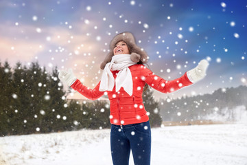 people, season and leisure concept - happy woman in fur hat having fun outdoors over snow and natural winter landscape background