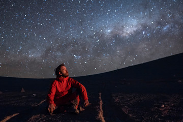 Wall Mural - a young adult man seating and looking at the view of our milky way galactic core located in the cons