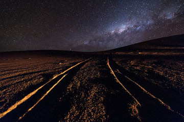 Wall Mural - a view of a dirt road with the track imprint in the sand going to the milky way on a starry night at