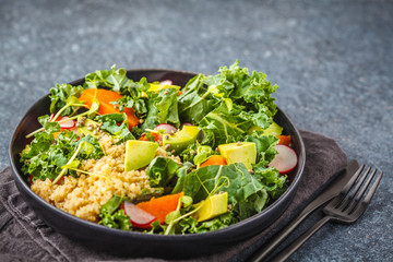 Avocado, quinoa, yam and kale salad in black plate on a dark background.