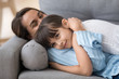 © fizkes - Close up little daughter lying on sofa hugging mother at home. Beautiful loving young mother gentle embrace adorable smiling child spend time together indoors. Lazy weekend happy motherhood concept