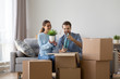 © fizkes - Married diverse couple sitting together on sofa in living room at new modern home unpack belongings from cardboard boxes wife hold flower pot, husband hold decorative glass bottle. Moving day concept