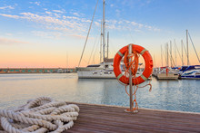 The Quay Of A Marina At  The Sunset /a Mooring Rope With A Lifebelt  On  The Quay Of A Marina At  The Sunset