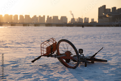 Fotografie, Obraz Deserted bike in a icy Hun river in Shenyang, China, whit beautiful sunset above