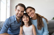© fizkes - Head shot happy diverse family sitting on couch have video call smiling looking at camera, small daughter spend time on weekend together with parents communicate with friends or relatives via internet