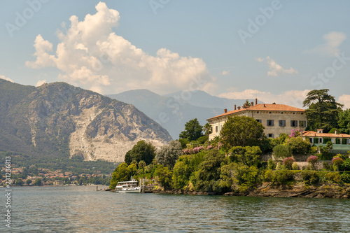 Fotografie, Obraz Veduta dal lago di un'isola con costa montuosa sullo sfondo e cielo blu con nubi
