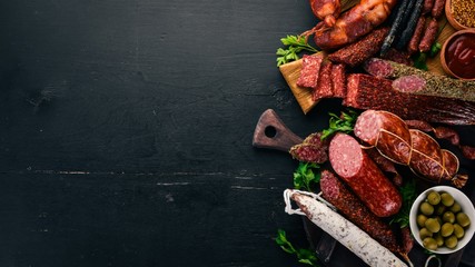 Wall Mural - Assortment of salami and snacks. Sausage Fouet, sausages, salami, paperoni. On a black wooden background. Top view. Free space for your text.