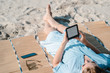 Frau liest mit E-Book Reader am Strand