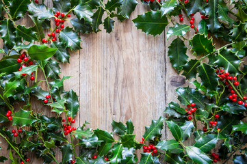 Seasonal background of weathered wood framed by sprigs of green Christmas holly with red berries