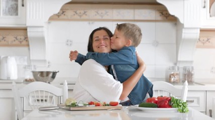 caring young mother and cute little son showing tenderness and love hugging in home kitchen