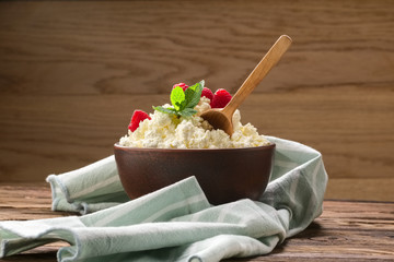 Wall Mural - Fresh cottage cheese with raspberries and wooden spoon in clayware on wooden table