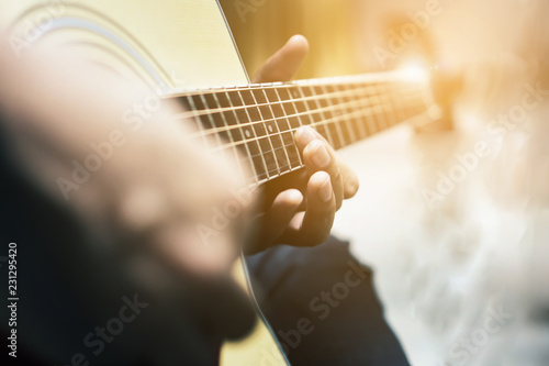 Fotografie, Obraz The man is playing guitar in the garden, Close-up male hand playing on acoustic guitar outdoor with bokeh and rays of sunlight