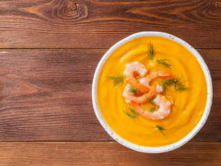 Wall Mural - delicious pumpkin cream soup with shrimp on dark brown wooden background, top view, copy space