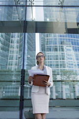 Wall Mural - The young business woman in gray office dress holds in hand folder with documents. Businesswoman standing next to the business center