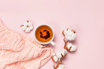 Wall Mural - Female pink knitted sweater, branch of cotton, cup of tea on pastel pink background top view flat lay. Lady winter Clothes fashion look. Delicate cotton flowers. Lifestyle gentle female background