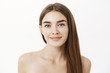 © Cookie Studio - Close-up shot of tender and feminine cute young woman with long brown hair standing naked over grey wall and smiling having no pimples being pleased with perfect pure skin condition over grey wall