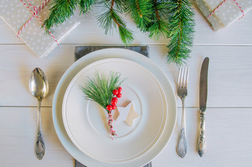 Wall Mural - Christmas table setting with traditional Christmas decoration in white red tone. Beautiful festive dinner background. Xmas tableware, plate  green fir branch and red berries