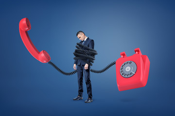 Wall Mural - a small businessman stands bound by a huge plastic cord from a giant red retro phone.