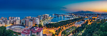 Night Aerial Panorama Of Malaga, Spain With Skyscrapers, Streets, Port, City Hall And Park During Golden Hour