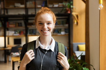 Wall Mural - Redhead lady student posing indoors in library istening music with earphones.