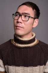 Young Asian man wearing turtleneck sweater against gray backgrou