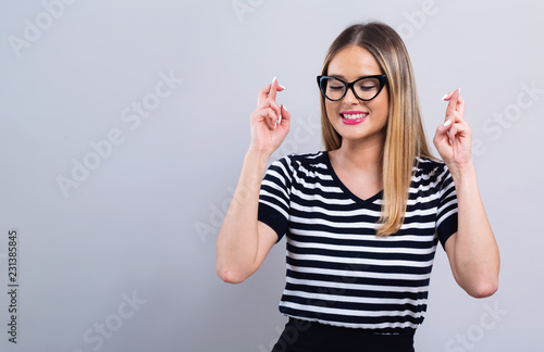 Fotomural Young woman crossing her fingers and wishing for good luck on a gray background