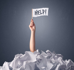 Female hand emerging from crumpled paper pile holding a white flag with help written on it