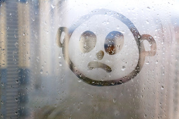 Foggy glass on window with drawn sad face concept photo with copyspace