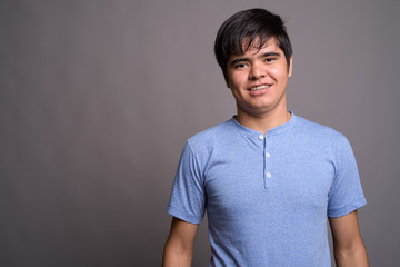 Young Asian teenage boy wearing blue shirt against gray backgrou