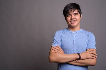 Wall Mural - Young Asian teenage boy wearing blue shirt against gray backgrou