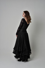 Canvas Print - full length portrait of brunette girl wearing long black lace gown with corset.  standing pose with back to the camera, grey studio background.