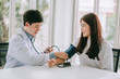 © chompoo - Doctor using sphygmomanometer with stethoscope checking blood pressure to a patient in the hospital.