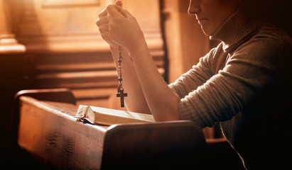 Wall Mural - Christian woman praying in church. Hands crossed and Holy Bible on wooden desk.