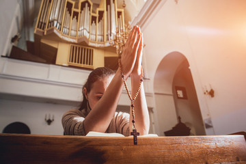 Wall Mural - Christian woman praying in church. Hands crossed and Holy Bible on wooden desk.