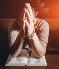 Wall Mural - Christian woman praying in church. Hands crossed and Holy Bible on wooden desk.