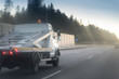 © Mak - A white car hauler truck with an empty two-tiered trailer for transporting cars is moving along the broadband scenic highway. road with metal safety and sound barrier