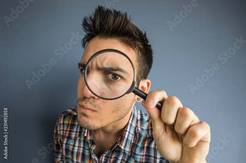 Photographie Funny man of a casual man looking though magnifyng glass on a grey background