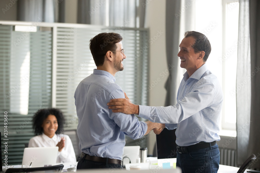 Smiling middle-aged ceo promoting motivating worker shaking hands congratulating with achievement promising respect bonus thanking for good work, team applauding, employee reward recognition concept - obrazy, fototapety, plakaty 