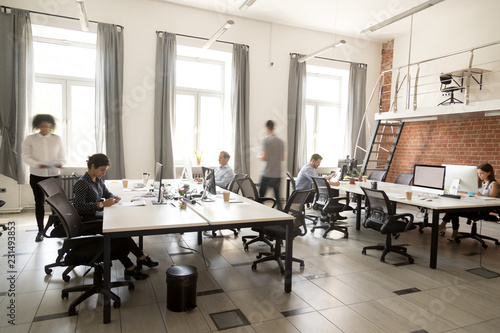 Fototapeta na szkło Pracownicy korporacji współpracują ze sobą przy użyciu komputerów w coworkingu, grupa zapracowanych pracowników chodzi w ruchu, siedzi przy biurkach w nowoczesnym wnętrzu pokoju o otwartej przestrzeni, koncepcja codziennego biura w pośpiechu