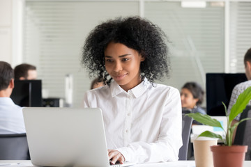 smiling young african female intern student worker working on laptop in modern office, focused black
