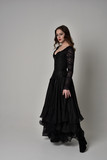 Fototapeta  - full length portrait of brunette girl wearing long black gown with corset. standing pose on grey studio background.