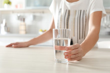 Woman Holding Glass With Clean Water On Table In Kitchen, Closeup