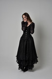 Fototapeta  - full length portrait of brunette girl wearing long black gown with corset. standing pose on grey studio background.