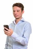 Fototapeta Na ścianę - Handsome serious Caucasian businessman holding mobile phone