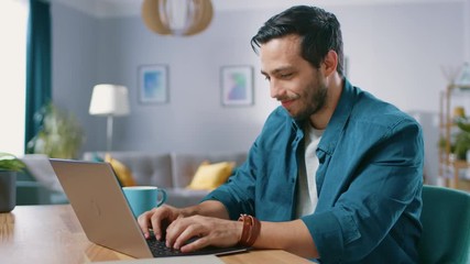 Wall Mural - Portrait of Handsome Young Man Using Laptop Computer at Home, Watching and Laughing at Content. Happy Hispanic Man Works on Computer.