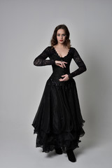 Sticker - full length portrait of brunette girl wearing long black gown with corset. standing pose on grey studio background.