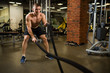 © terentiewshura - Athletic muscular man engaged with a thick rope with a bare torso in the gym.